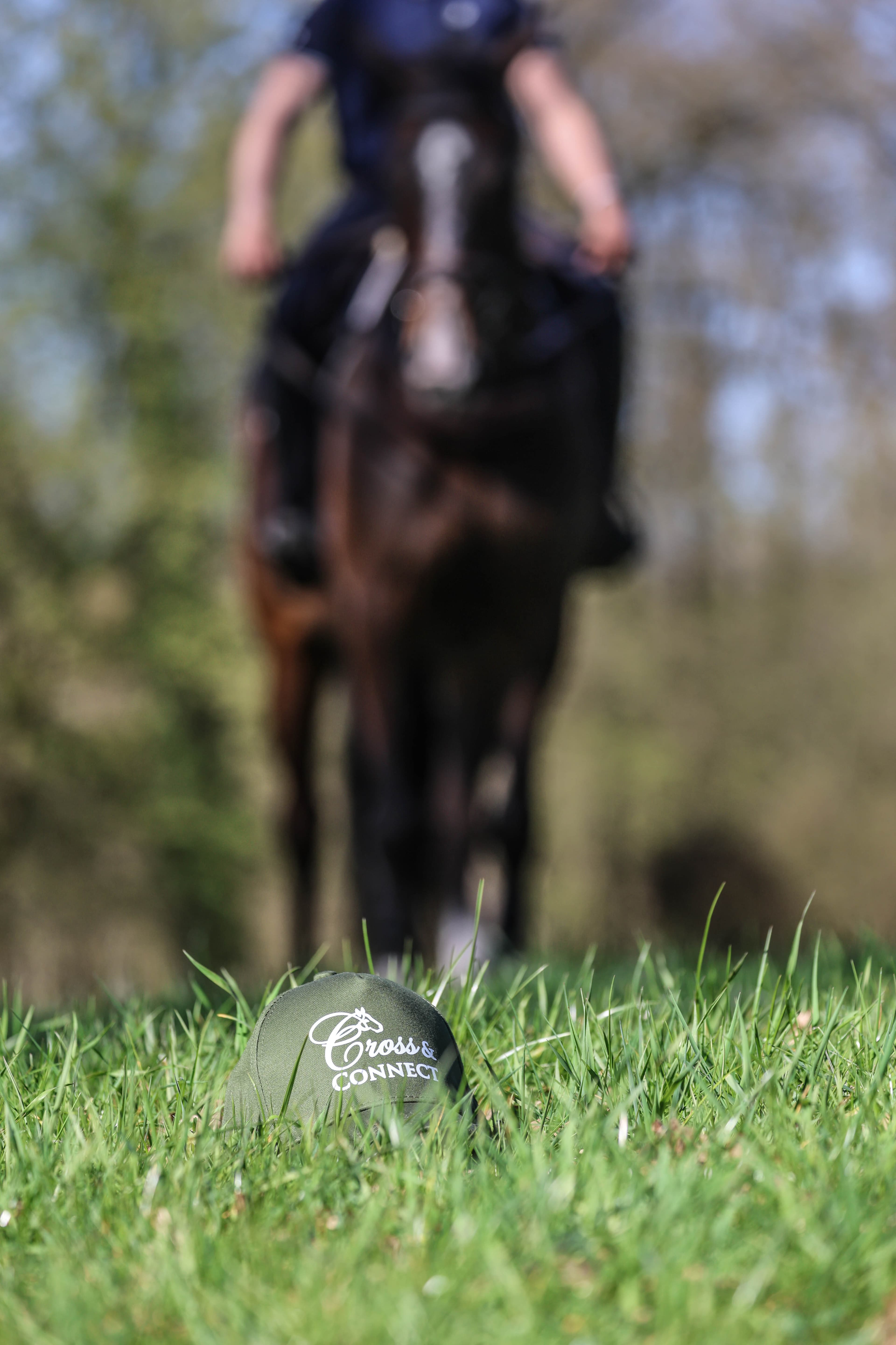 Two riders cantering side by side along a grass track beside the woods.